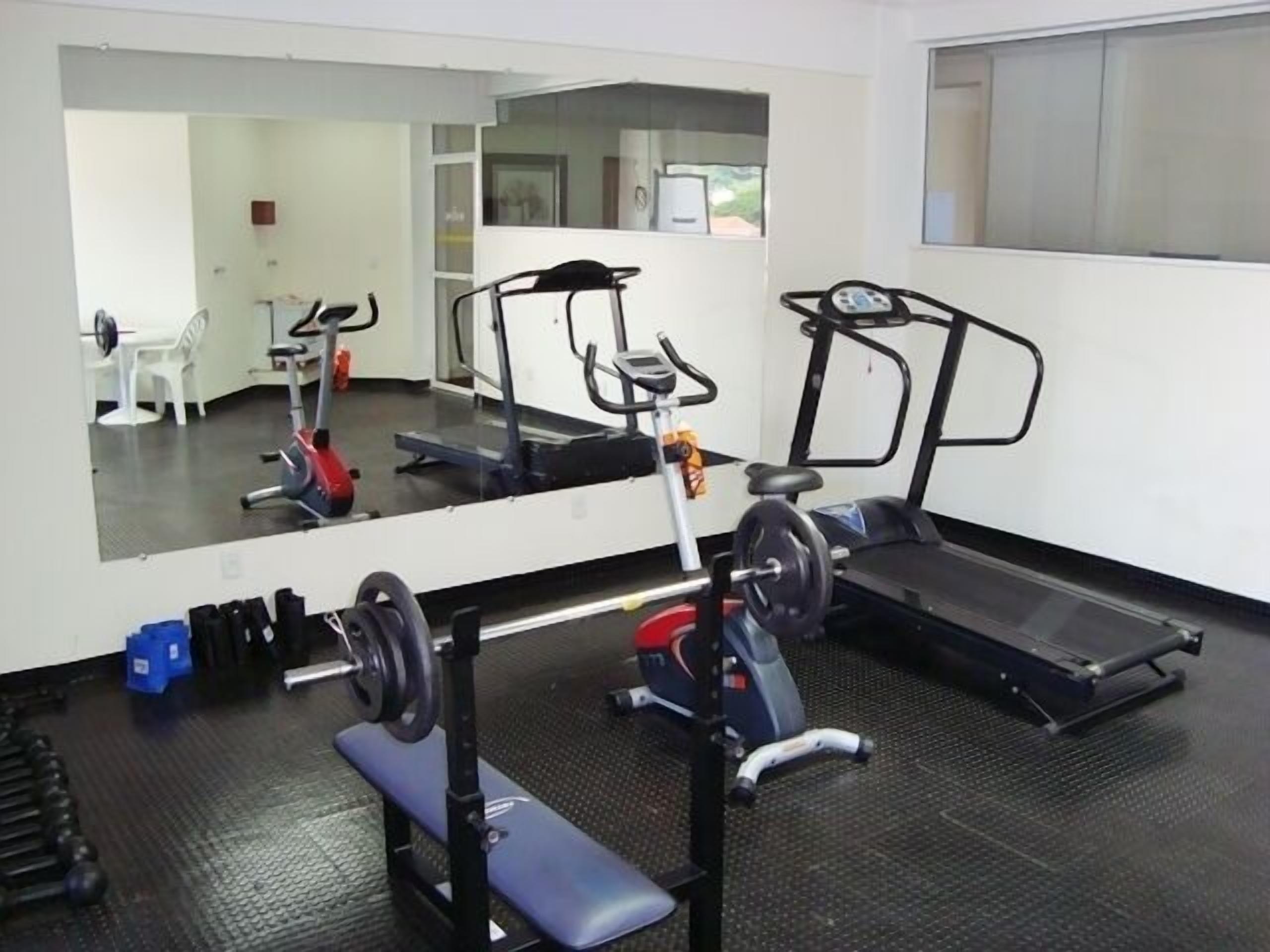 A gym with a treadmill, weight bench, and mirrored wall.