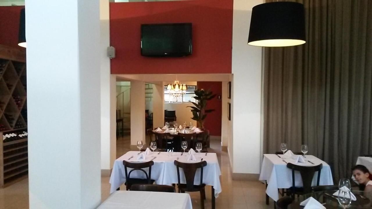 Un coin repas avec des tables préparées pour deux personnes, un téléviseur fixé au mur et un lustre.