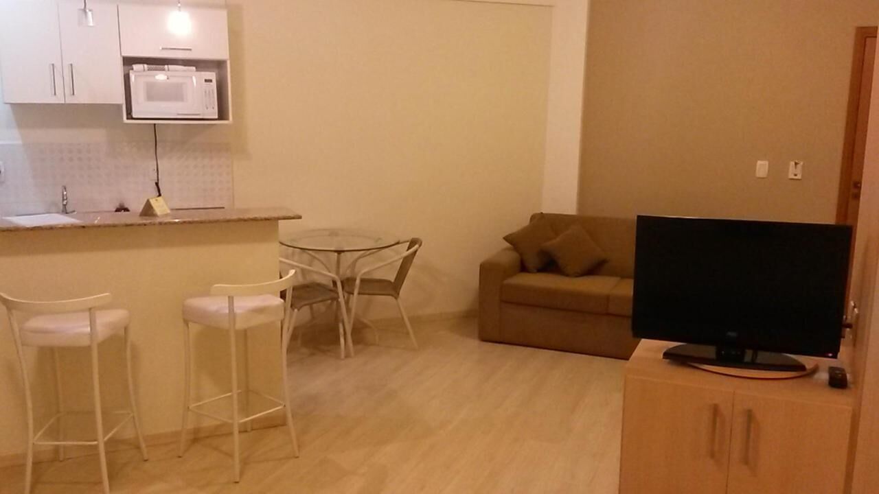 A compact living space with a kitchenette, a dining area with a glass table and chairs, a sofa, and a television on a wooden cabinet.