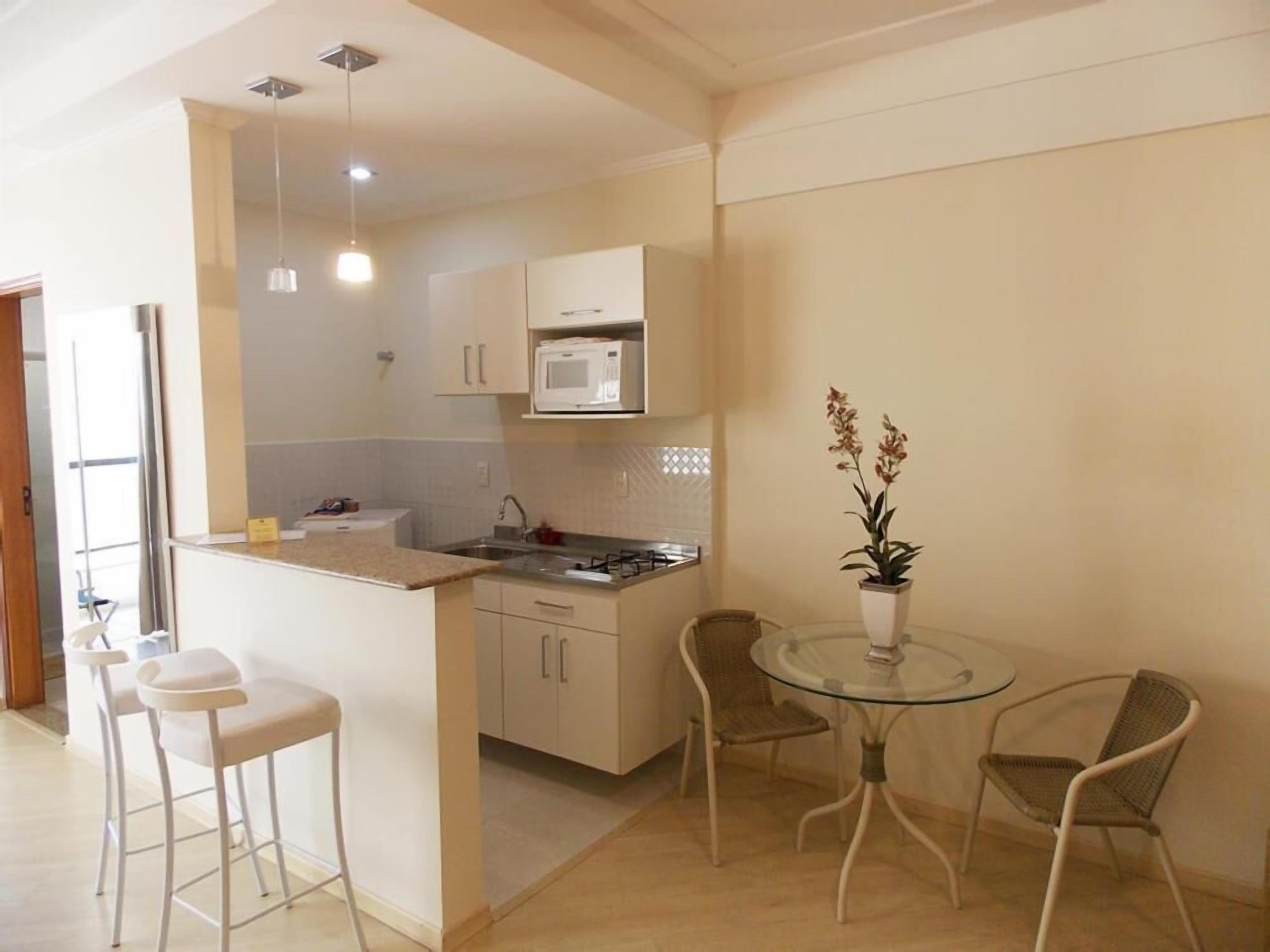 A compact kitchen with white cabinets, a microwave, and a small dining area with two chairs and a glass table.