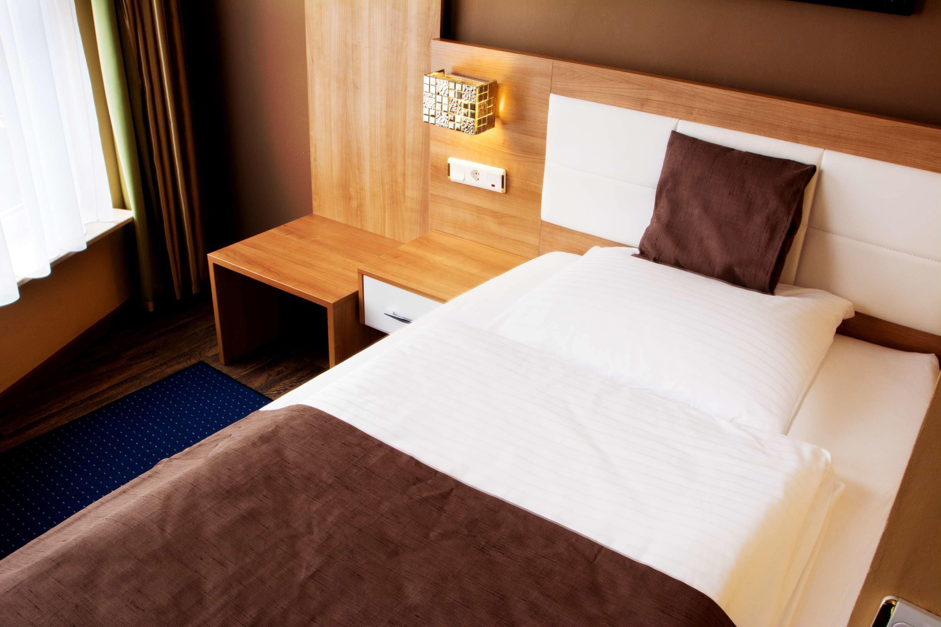 A hotel room with a bed, a nightstand, a lamp, and a window with curtains.