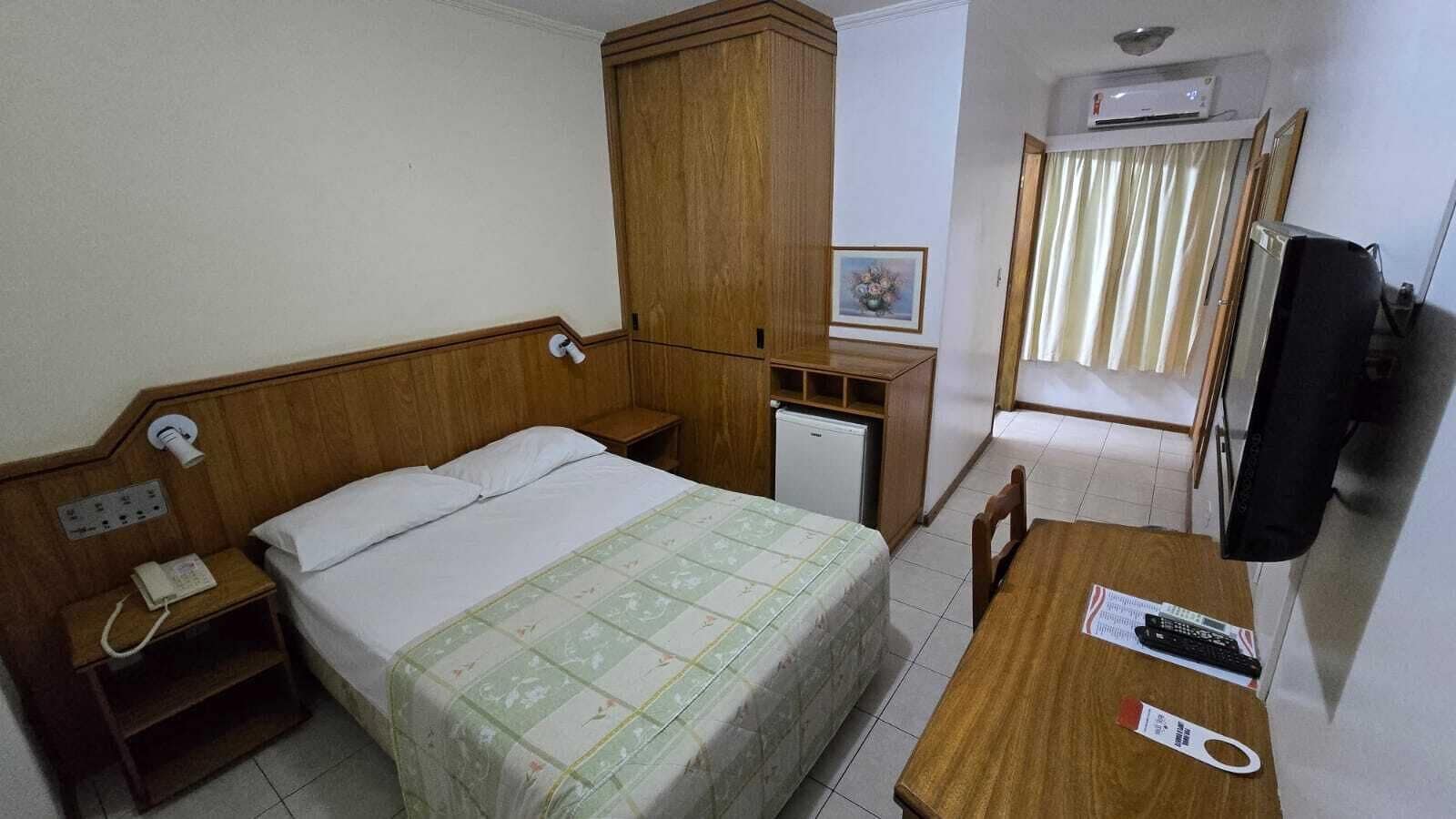 A hotel room with a bed, a desk, a chair, a telephone, a television, and a wardrobe.
