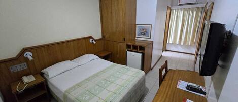 A hotel room with a bed, a desk, a chair, a telephone, a television, and a wardrobe.