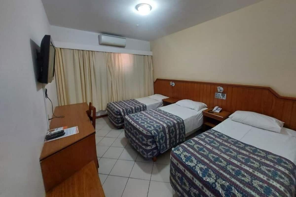 A hotel room with three beds, a desk, a television, and an air conditioning unit.