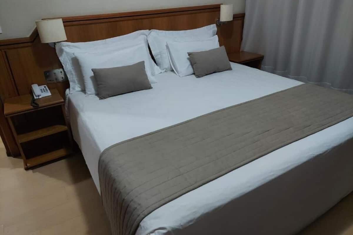 A hotel room with a large bed, a bedside table with a lamp, a phone, and a nightstand.