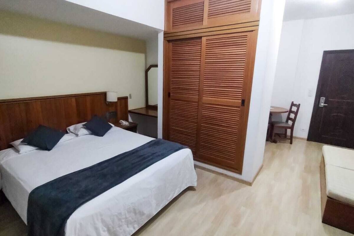 A hotel room with a bed, bedside tables, a wardrobe, a desk, and a chair.