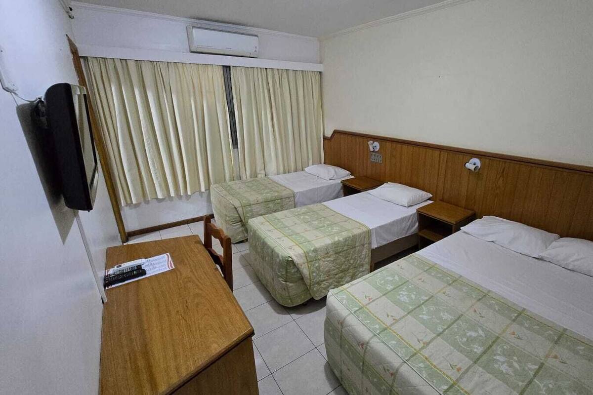A hotel room with two single beds, a wooden desk, a chair, a television, and a window with curtains.