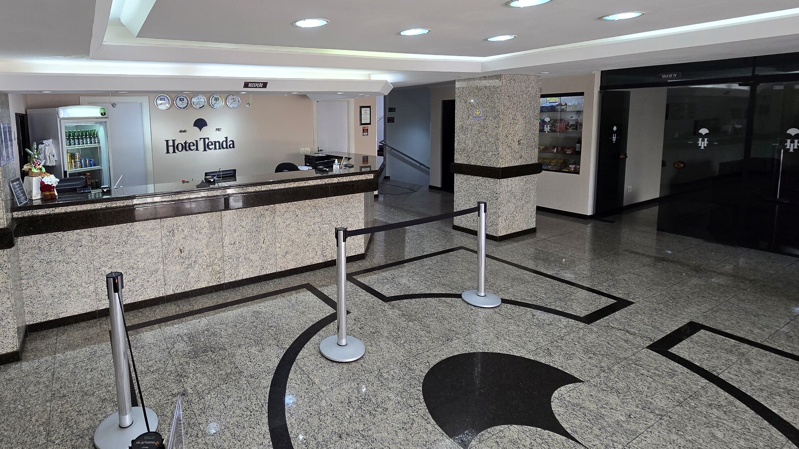Zona de recepción de un hotel, con mostrador de recepción, un reloj y un cartel que indica la recepción.