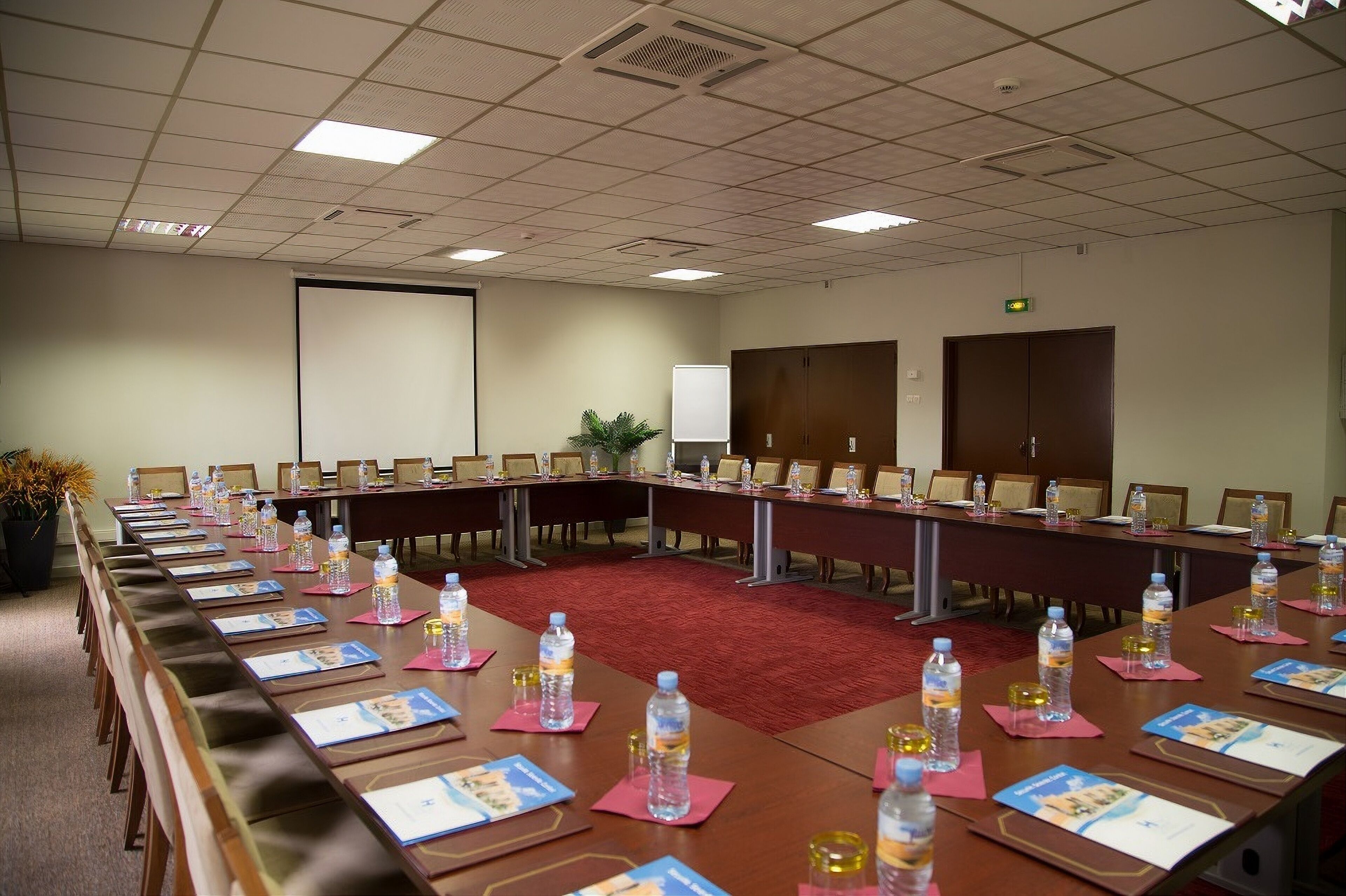 Un salón de conferencias con mesas largas, sillas, botellas de agua y tarjetas de identificación.