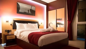 A neatly made bed with white linens and a red accent, a bedside table with a lamp, and a large window with red curtains. - Monotel Dar El Barka (Nouakchott)