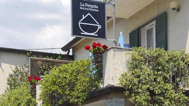 A sign for "La Pergola Bed and Breakfast" with a balcony featuring potted red flowers and green shrubs. - La Pergola (Vezzano Ligure)