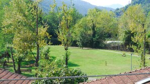 A view of a park with a grassy area and trees, a bench, and a building with a tiled roof in the foreground. - La Pergola (Vezzano Ligure)