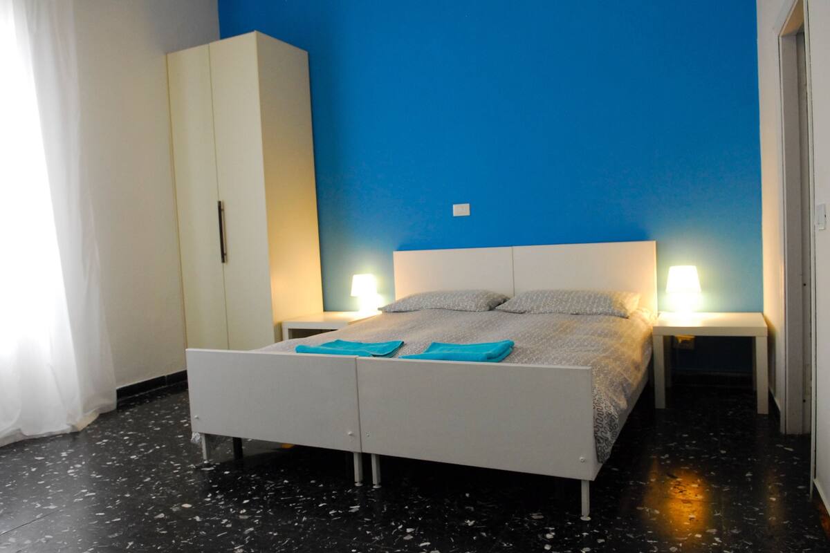 A bedroom with a bed, two bedside tables, a wardrobe, and a blue wall.