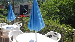 Outdoor seating with blue umbrellas, white plastic chairs, and a sign for 'La Pergola Bed and Breakfast'. - La Pergola (Vezzano Ligure)