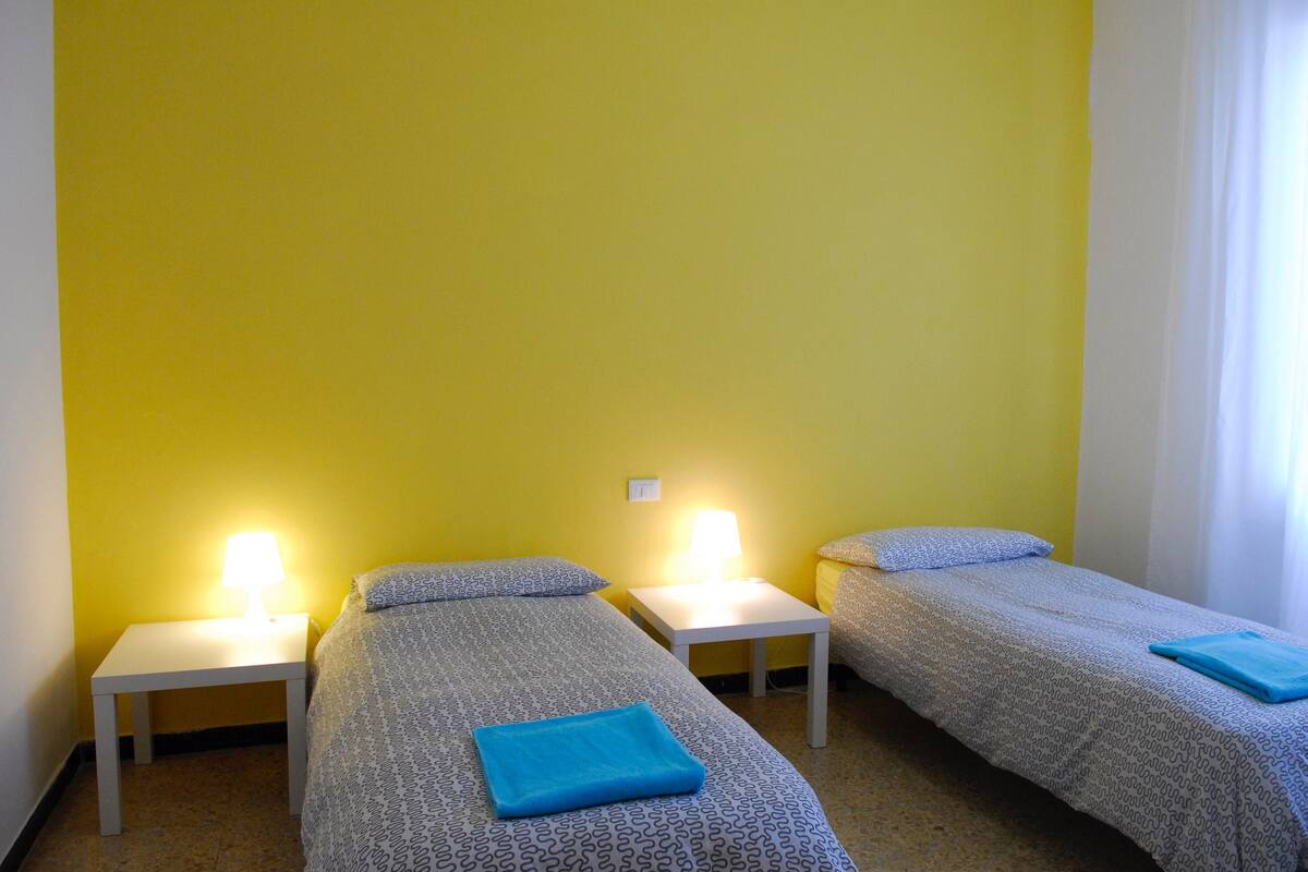 A room with three beds, each with a white nightstand and a lamp.