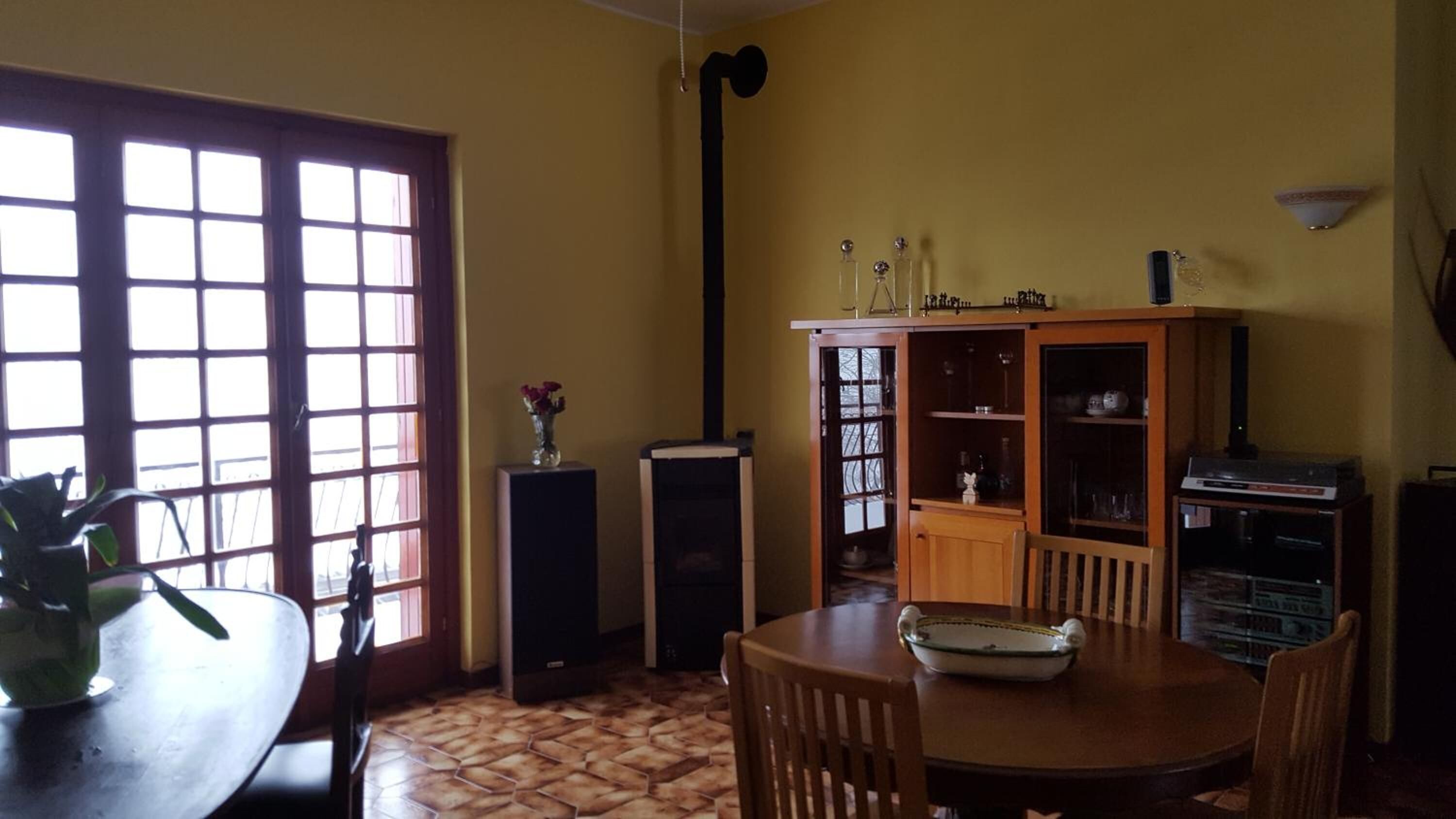 Un área de comedor con una mesa de madera, sillas, un aparador con puertas de vidrio y un amplio ventanal con múltiples vidrios.
