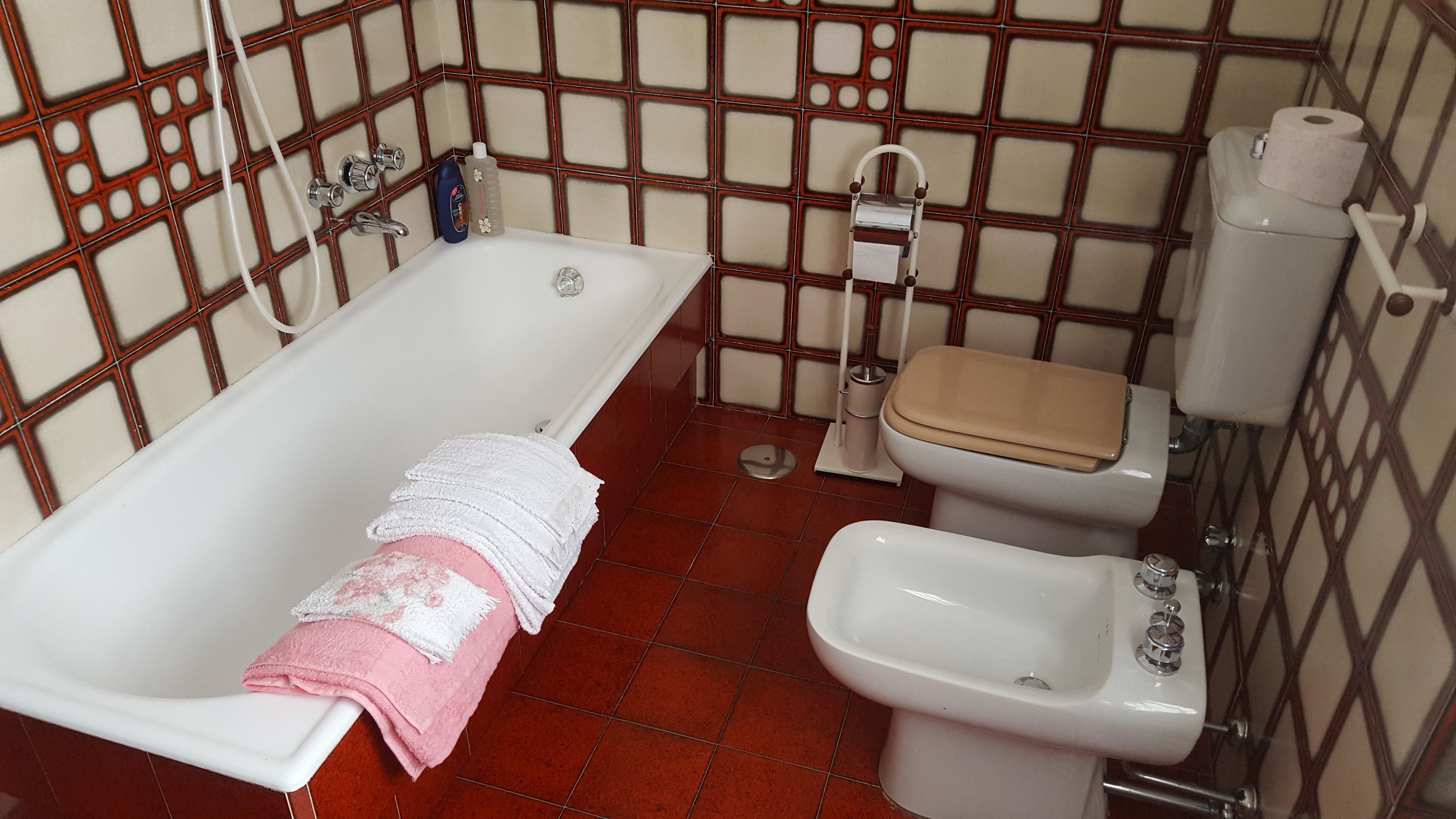 A bathroom with a bathtub, toilet, bidet, and tiled walls.