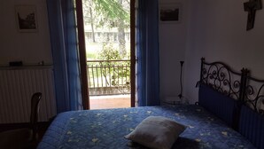 Een slaapkamer met een bed, een stoel, een radiator en een raam met gordijnen.