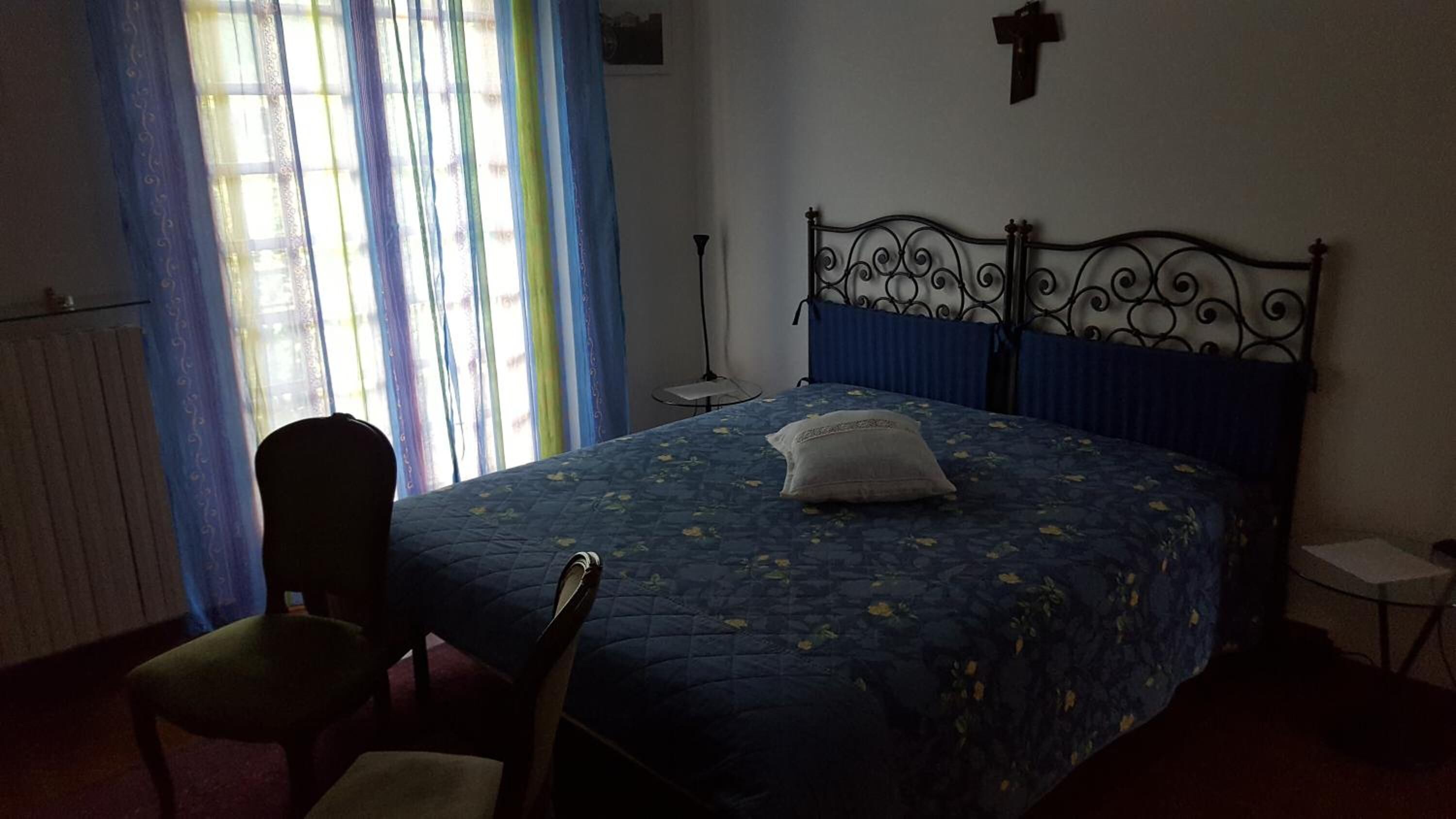 Een slaapkamer met een bed, een stoel, een nachtkastje, een lamp en een raam met gordijnen.