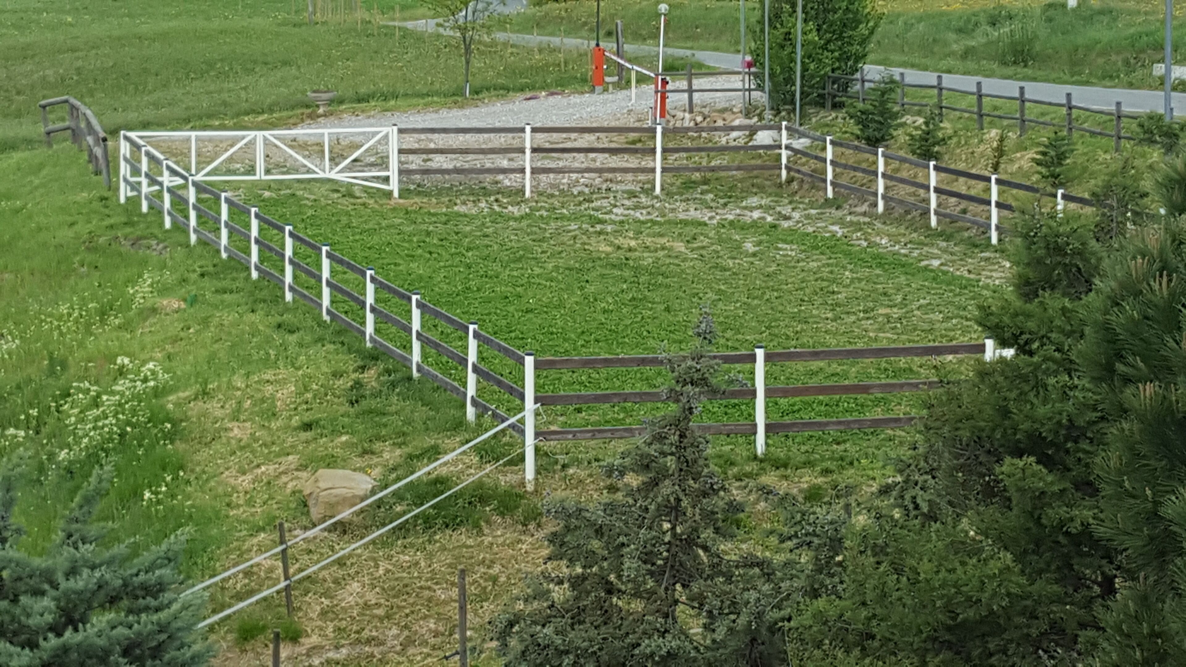 Un espacio exterior cercado con un sendero de grava, rodeado de vegetación y una pequeña colina.