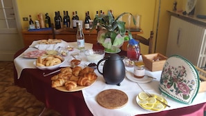 Een ontbijttafel met croissants, brood, een koffiekan, een kan sap en een bord met citroenpartjes.