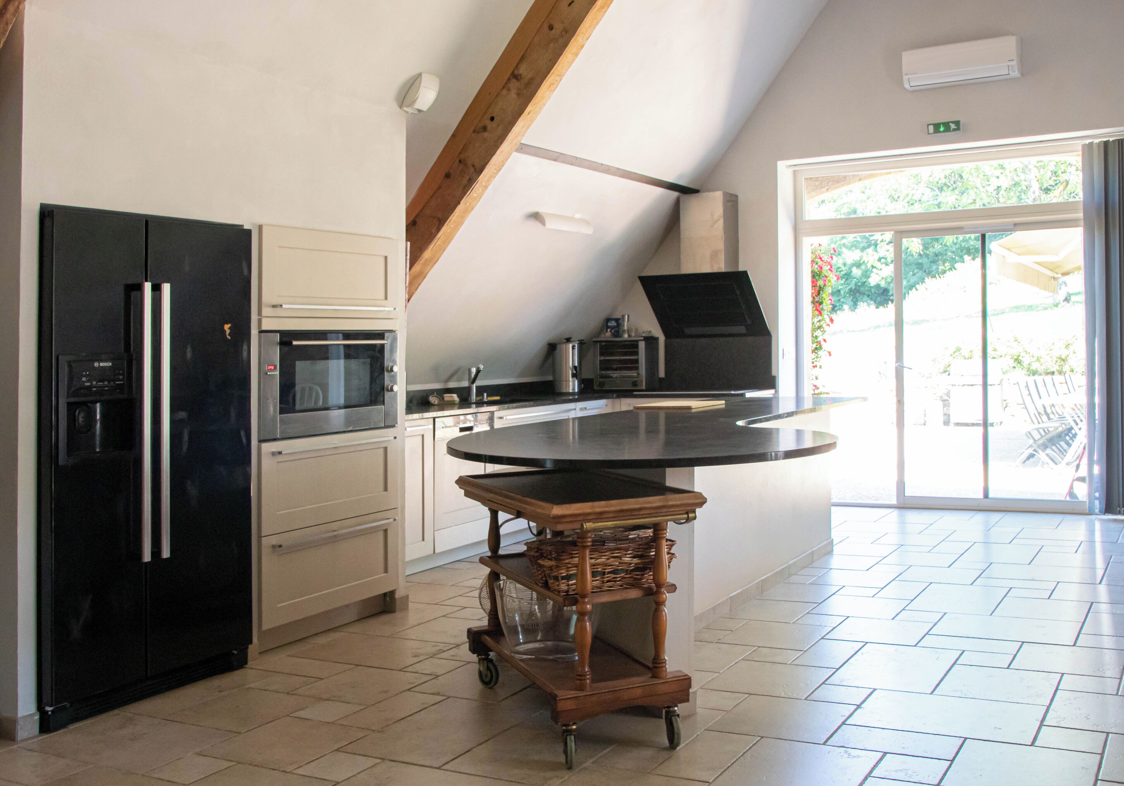 A kitchen with a black refrigerator, a microwave, a wooden cart, and a large island.
