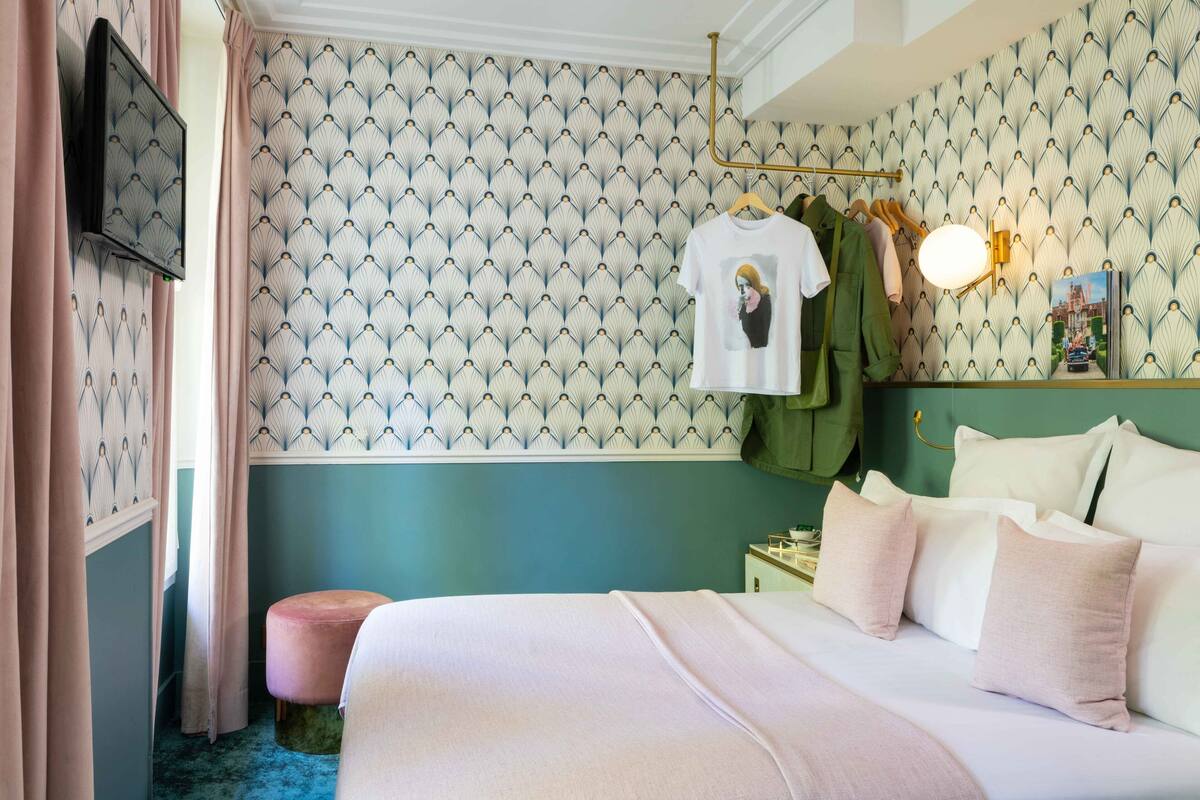 A bedroom with a bed, a hanging light, a wall-mounted TV, and a patterned wallpaper.