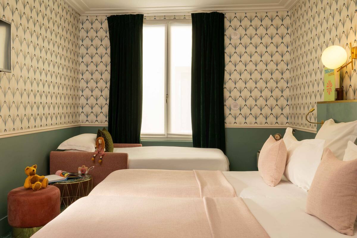 A hotel room with two beds, a small round table, a teddy bear, and a lamp.