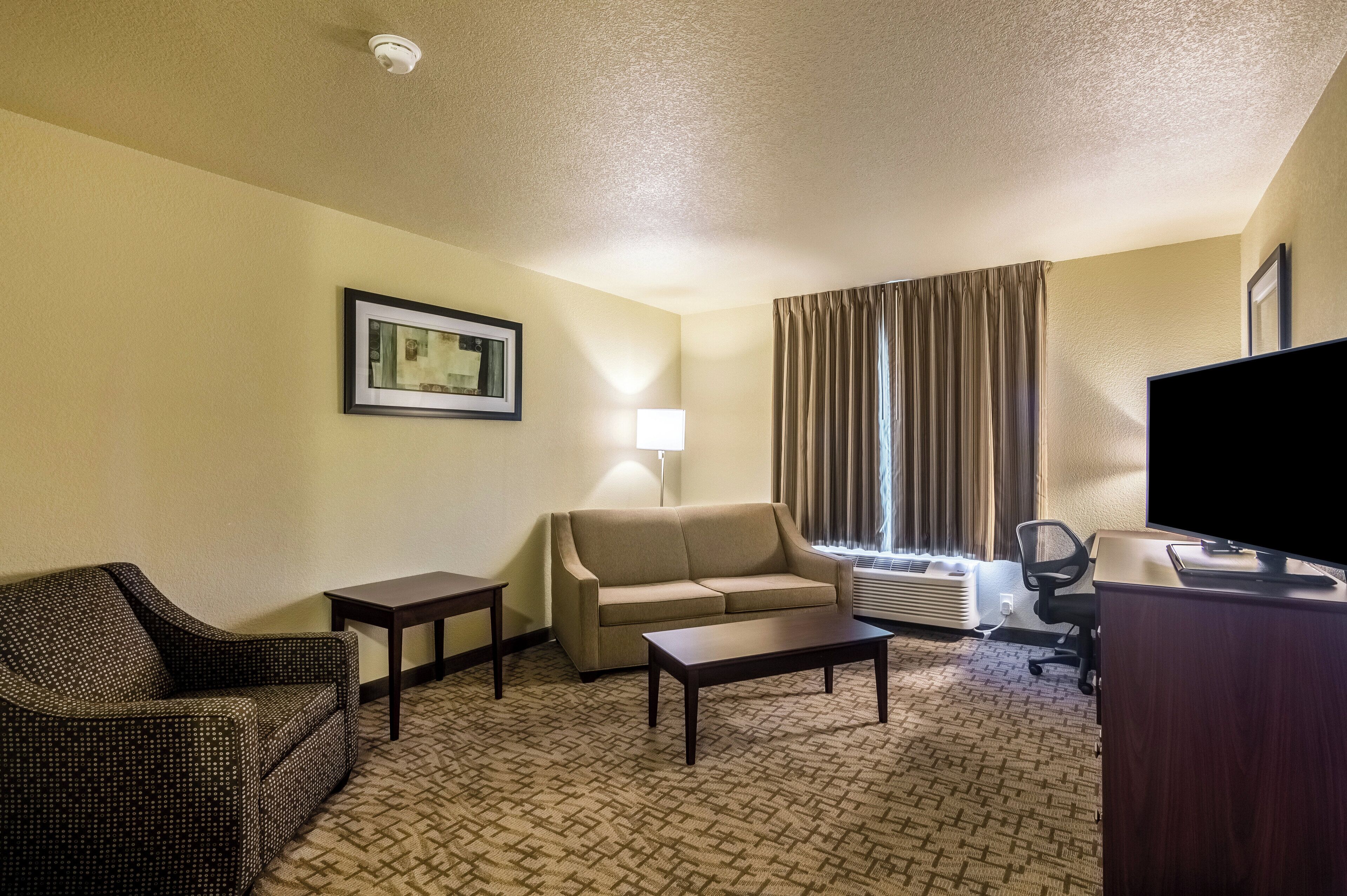 A hotel room with a sofa, a chair, a coffee table, a TV, and a lamp.
