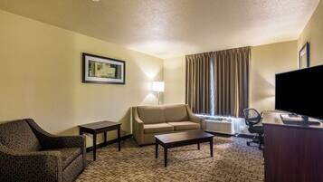 A hotel room with a sofa, a chair, a coffee table, a TV, and a lamp.