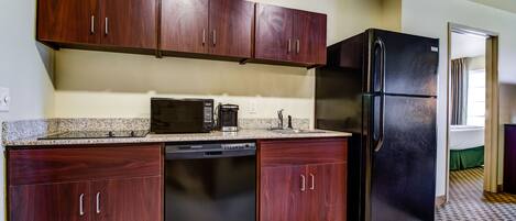 A kitchen with dark wood cabinets, a black refrigerator, a dishwasher, and a microwave.