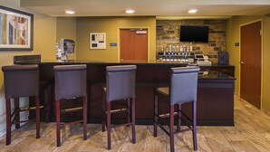 A bar area with a stone wall, a flat-screen TV, and a counter with stools. - Cobblestone Inn & Suites - Lakin (Lakin)