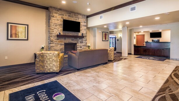 A spacious lobby with a stone fireplace, a sofa, and a reception desk. - Cobblestone Inn & Suites - Lakin (Lakin)