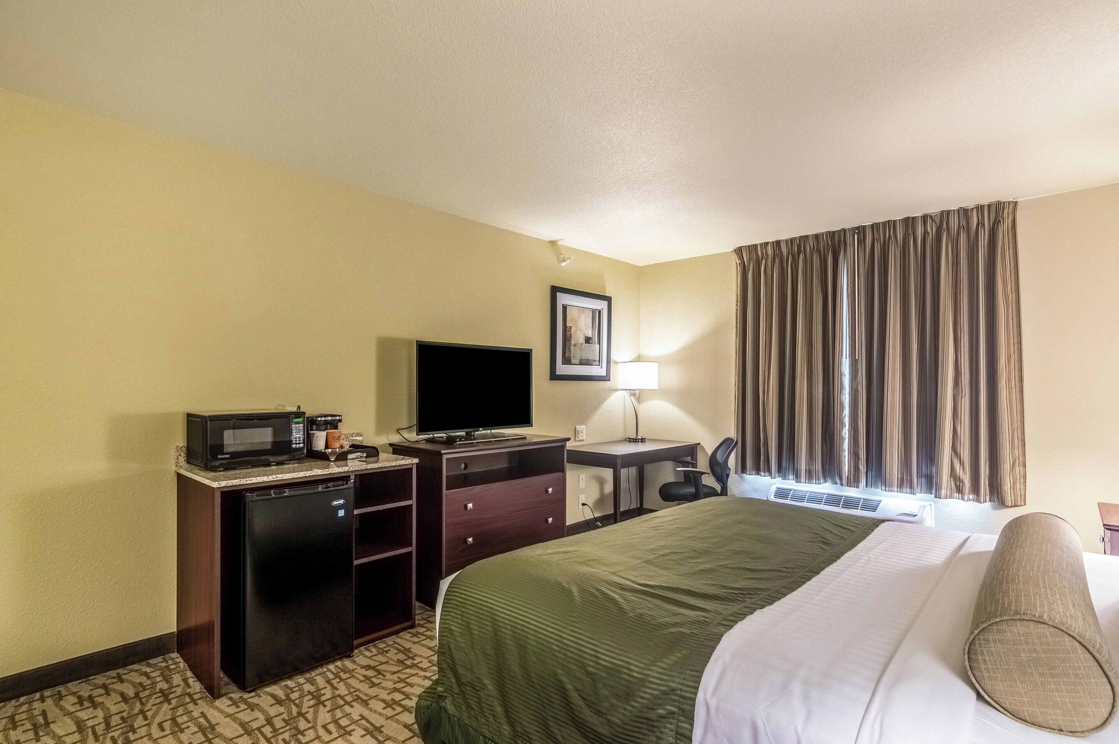 A hotel room with a bed, a desk with a computer, a television, a microwave, and a small refrigerator.
