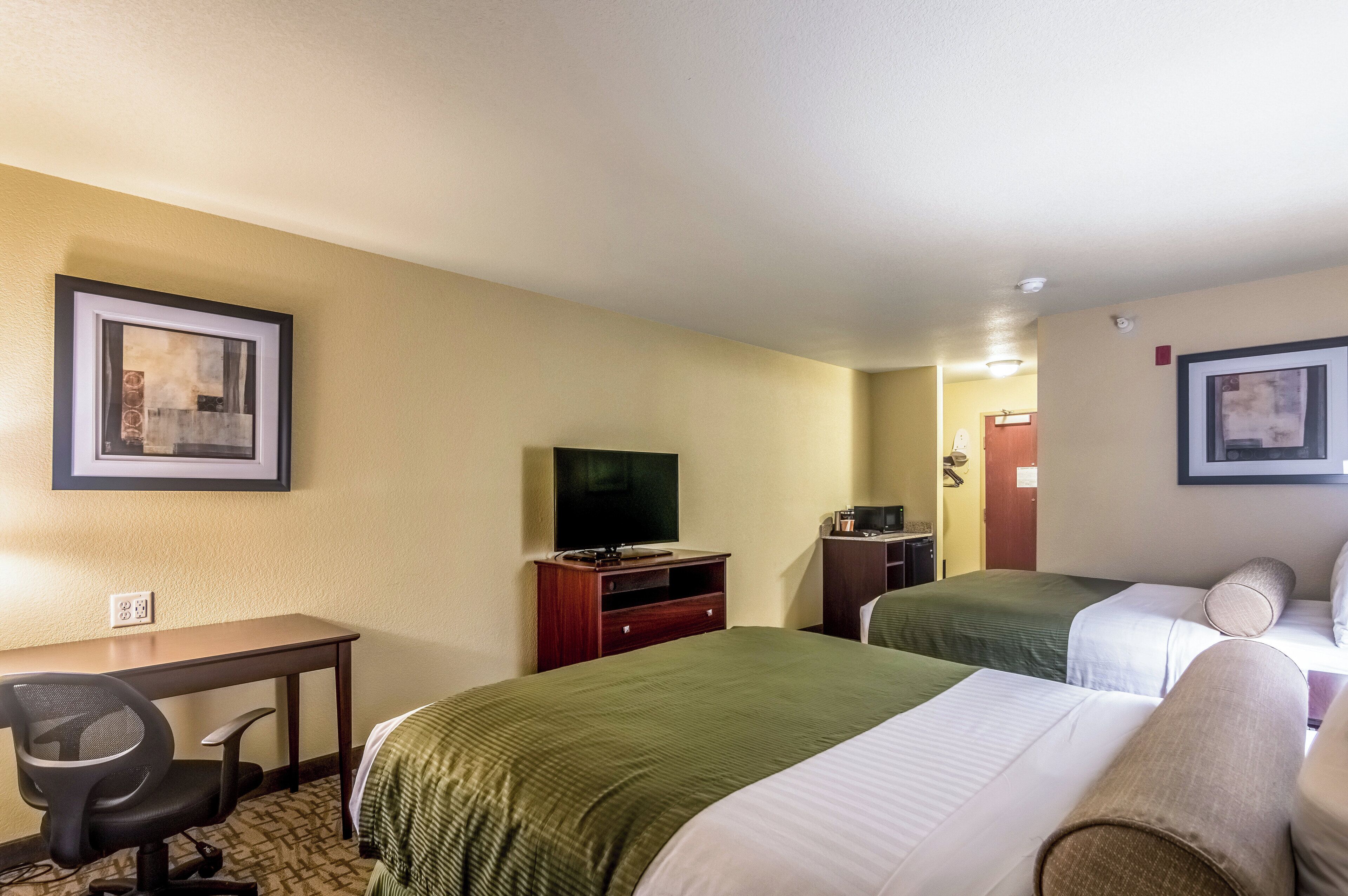 A hotel room with two single beds, a desk with a chair, a television, and a small desk with a computer.