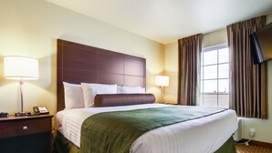 A hotel room with a large bed, two bedside lamps, a flat-screen TV, and a window with curtains. - Cobblestone Inn & Suites - Lakin (Lakin)