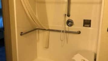 Een douchecel met een handgreep, een handdouche en een klein krukje.