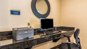 A hotel business center with a desktop computer, printer, and a sign indicating the location.