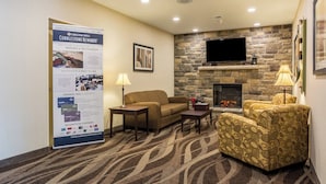 Eine Hotelhalle mit Kamin aus Stein, einem Flachbildfernseher, einer Couch, einem gemusterten Sessel und einem Plakat, das die Hotel-Treueprogramm bewirbt.