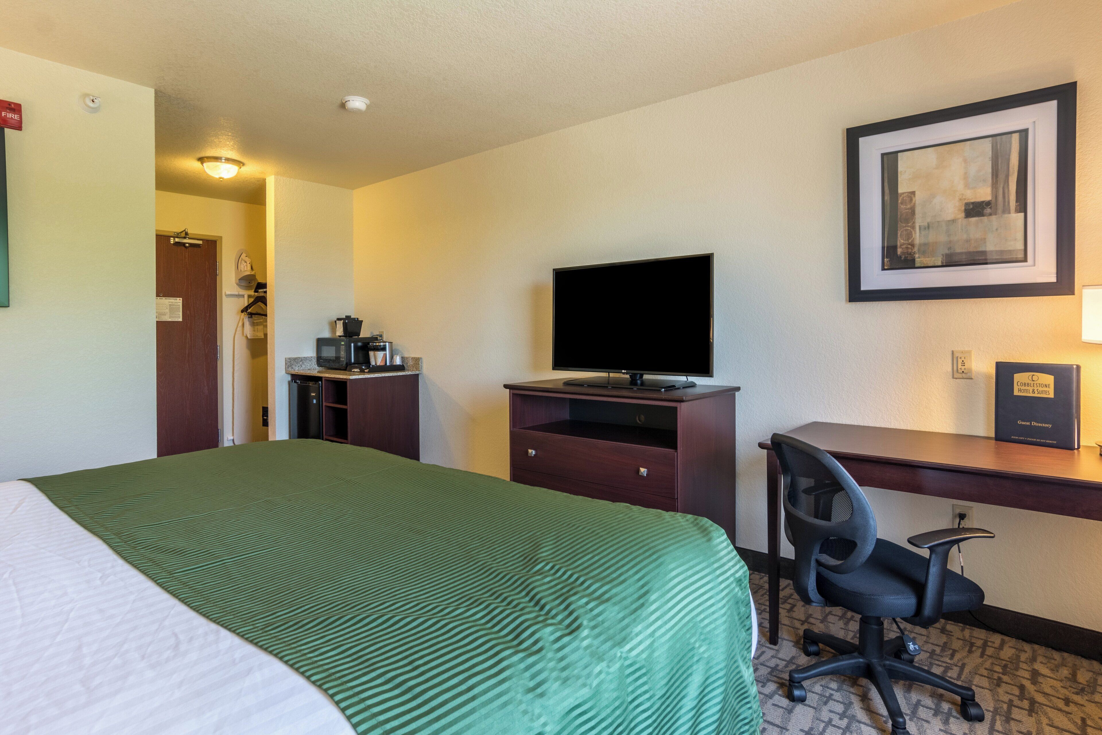 A hotel room with a bed, a desk with a computer, a television, and a coffee maker.