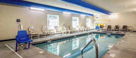 An indoor swimming pool with clear lanes, blue and white chairs, and a lifeguard chair.
