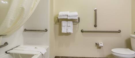 A bathroom with a bathtub, a toilet, a handrail, and a towel rack.