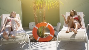 Dos sillones de relax con un anillo salvavidas entre ellos, una palmera y una pared blanca.
