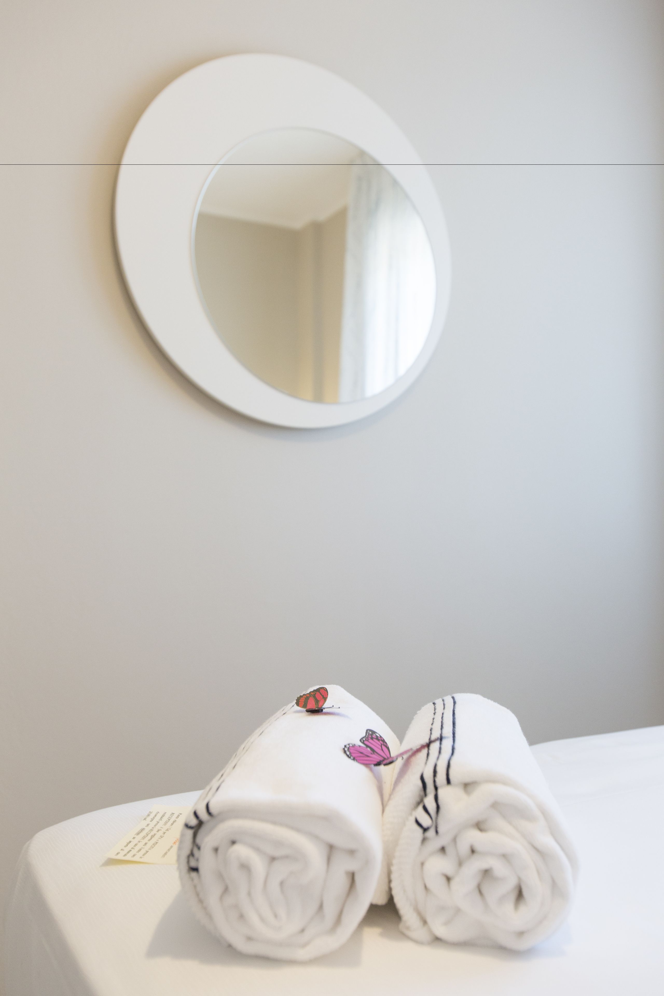 Una cama bien hecha con dos toallas enrolladas y un espejo redondo en la pared.