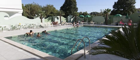 Una piscina al aire libre, sombrillas, sillones reclinables de piscina