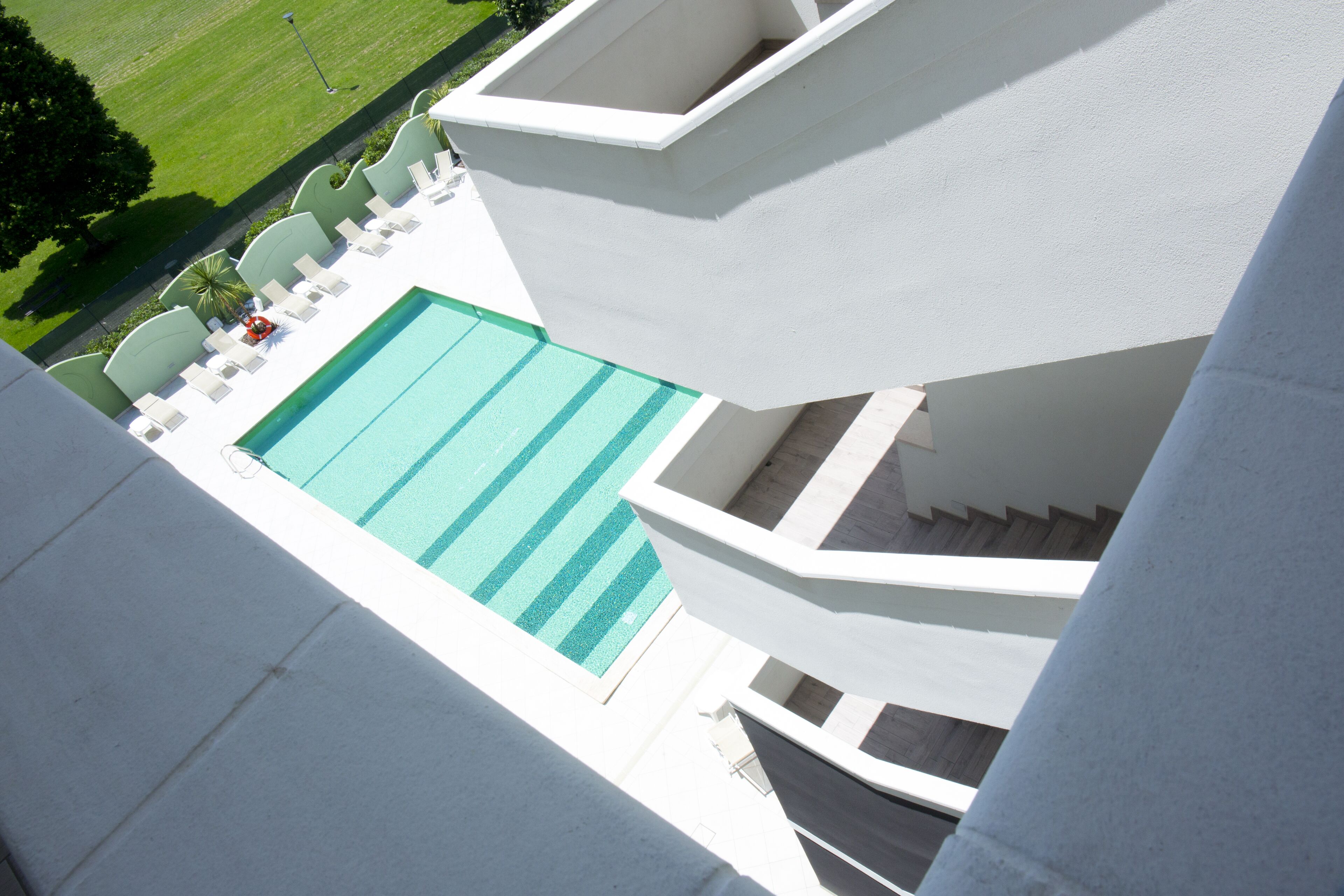 A pool area with a clear view of the water, a set of white lounge chairs, and a staircase leading to an upper level.