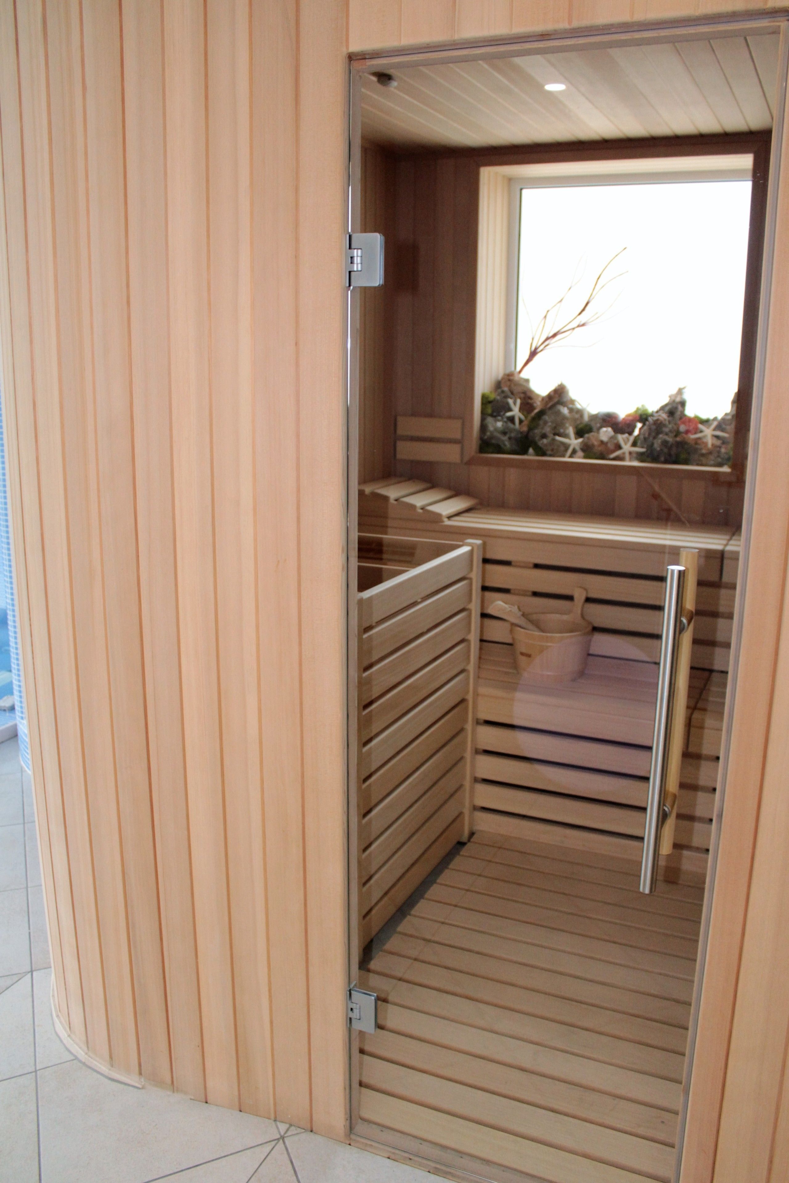 Eine Holzhütte als Sauna mit einer Rippenholzboden und einem Fenster mit dekorativem Blick auf Steine und Muscheln.
