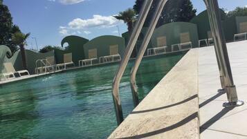 A swimming pool with clear water, surrounded by lounge chairs and a metal pool ladder.