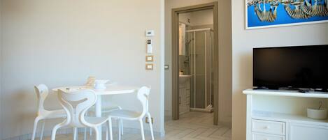 A modern room with a dining table and chairs, a TV, and a shower area.