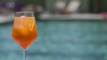 Ett cocktailglas med en klar vätska och isbitar, placerat på en vit yta nära en pool med en suddig bakgrund.